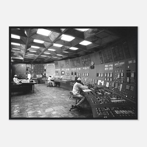Könnte beinhalten: Ein Schwarz-Weiß-Foto eines großen industriellen Kontrollraums mit einer gitterartigen Decke, mehreren Arbeitsplätzen mit komplexen Konsolen und mehreren Personen in hellen Uniformen, die die Geräte bedienen.