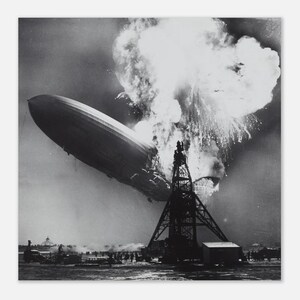 May include: A monochrome image depicting the Hindenburg airship engulfed in flames. The airship is falling, with a large explosion at the rear. A tall metal structure and a crowd of people are seen below the airship.