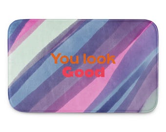 Puede incluir: Alfombra de baño rectangular con un diseño de acuarela en tonos azules, morados, rosas y blancos. Las palabras "You look Good" están impresas en naranja y rojo en la alfombra.