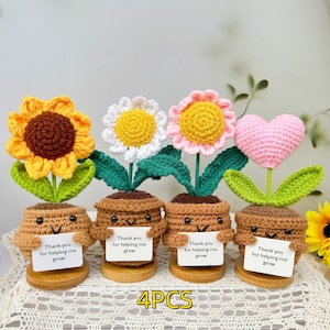 Könnte beinhalten: Set aus vier gehäkelten Blumentöpfen mit verschiedenen Blumendesigns, darunter eine Sonnenblume, eine Gänseblümchen, ein Herz und eine gelbe Blume. Jeder Topf hat ein lächelndes Gesicht und hält ein Schild mit der Aufschrift "Danke, dass du mir beim Wachsen hilfst".