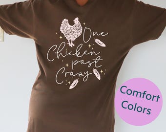 May include: Brown t-shirt with a white graphic of a chicken and the text "One chicken past crazy".