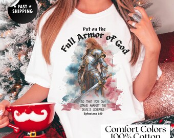 Op de afbeelding: Wit T-shirt met een afbeelding van een krijger in zilveren harnas, een zwaard en de tekst "Put on the Full Armor of God". Het shirt heeft ook de tekst "Comfort Colors 100% Cotton".