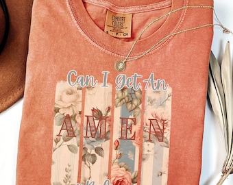以下が含まれることがあります： コーラル色のTシャツに、花柄のデザインと「Can I get an Amen #Believer」の文字がプリントされています。
