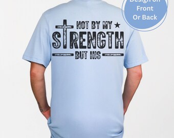 Può includere: Maglietta blu chiaro con una croce nera e il testo "Not by my strength but his" stampato sul retro.