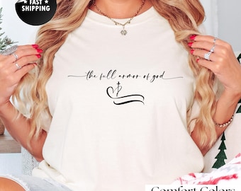 Op de afbeelding: Crèmekleurig T-shirt met de tekst "the full armor of god" in een scriptlettertype, samen met een kruis en een gebogen lijnontwerp. Het shirt is gemaakt van 100% katoen en heeft onderaan de tekst "Comfort Colors".