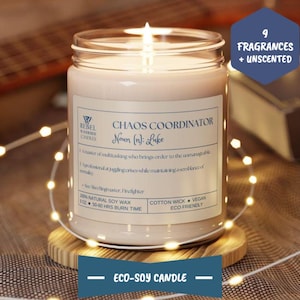 May include: A glass jar candle with a white label that reads "Chaos Coordinator Noun (n): Luke" and a definition of the term. The candle is on a wooden coaster and surrounded by white fairy lights. The label also states "100% Natural Soy Wax, 1 oz, 50-60 Hrs Burn Time, Cotton Wick, Vegan, Eco Friendly".