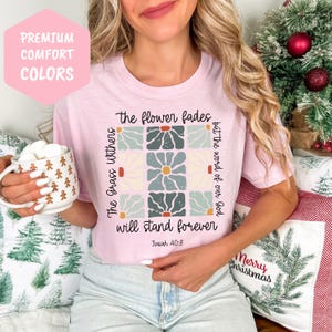 May include: A pink t-shirt with a floral design and the text "The flower fades but the word of our God will stand forever Isaiah 40:8".