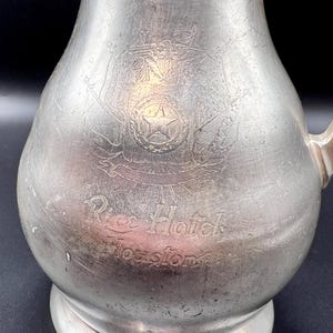 May include: A white ceramic mug with a black handle and the text "But First, Coffee" in a bold, black font. The mug is set against a blurred background, highlighting its clean design.