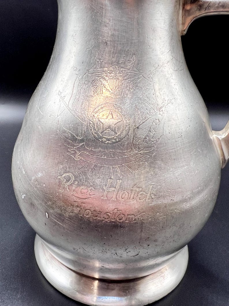 May include: A white ceramic mug with a black handle and the text "But First, Coffee" in a bold, black font. The mug is set against a blurred background, highlighting its clean design.