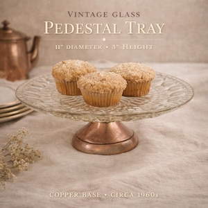 May include: Vintage glass pedestal tray with a copper base, circa 1960s. The clear glass tray is 11 inches in diameter and 3 inches high. Three muffins sit on the tray. The text on the image reads "Vintage Glass Pedestal Tray".