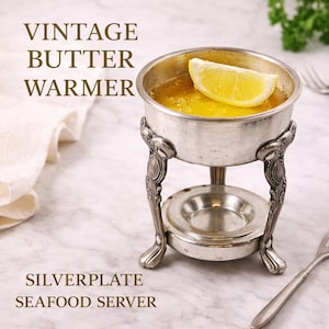 May include: A vintage silver-plated butter warmer with a lemon wedge garnish. The server has ornate legs and a small dish below. The text on the image reads "VINTAGE BUTTER WARMER" and "SILVERPLATE SEAFOOD SERVER".