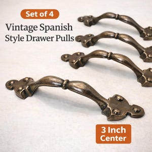May include: Set of four vintage Spanish-style drawer pulls. The bronze-colored handles have a curved design with decorative end pieces. The text indicates a 3-inch center measurement.
