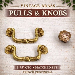 May include: Vintage brass pulls and knobs set. The image shows two matching pulls and one knob. The pulls have a curved design with floral accents, and the knob has a floral pattern. The pulls are 2.75 inches CTC. The style is French Provincial.