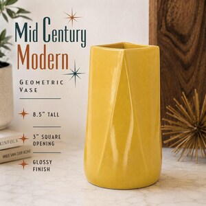 May include: A mustard yellow ceramic vase with a geometric, faceted design and a glossy finish. The text on the image reads: Mid Century Modern Geometric Vase, 8.5" tall, 3" square opening, glossy finish. The vase has a square-shaped opening.