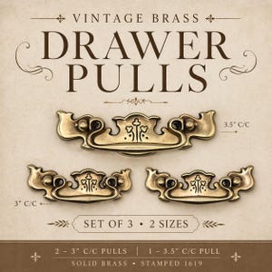 May include: Vintage brass drawer pulls in two sizes, with a set of three. The pulls have an ornate design with a cross-like emblem in the center. The larger pull measures 3.5 inches center to center, and the smaller pulls are 3 inches center to center.