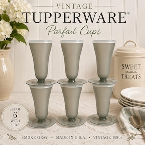 May include: A set of six vintage Tupperware parfait cups in a smoke gray color. Each cup features a flared base, a slender stem, and a matching translucent lid. The cups are arranged in two rows of three, showcasing their classic design.