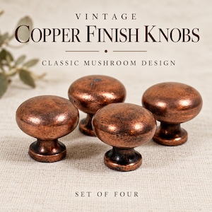 May include: A set of four mushroom-shaped knobs with a distressed copper finish. The text VINTAGE COPPER FINISH KNOBS, CLASSIC MUSHROOM DESIGN, and SET OF FOUR is displayed above and below the hardware items.