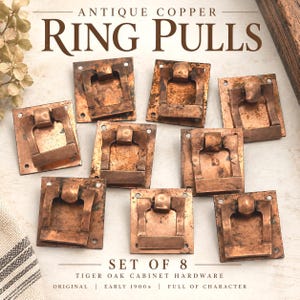 May include: A set of eight antique copper ring pulls for cabinet hardware. Each square backplate features a hinged drop handle with a weathered, metallic finish. The text on the image reads: ANTIQUE COPPER RING PULLS, SET OF 8, TIGER OAK CABINET HARDWARE, ORIGINAL, EARLY 1900S, FULL OF CHARACTER.