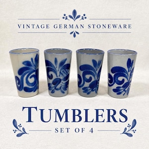 May include: A set of four vintage German stoneware tumblers featuring a light gray base with hand-painted cobalt blue floral patterns. The text VINTAGE GERMAN STONEWARE and TUMBLERS SET OF 4 is displayed in blue lettering above and below the four cups.