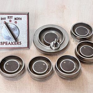 May include: A collection of vintage audio equipment components. Includes a control panel with "INT", "EXT", and "BOTH" settings, and the word "SPEAKERS". There are also several silver-toned knobs with dark brown centers.