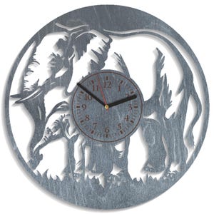 May include: A grey wooden wall clock with a cut-out design of an elephant and a baby elephant. The clock face is a dark grey with black hands and red numbers. The clock is round and has a natural wood grain.