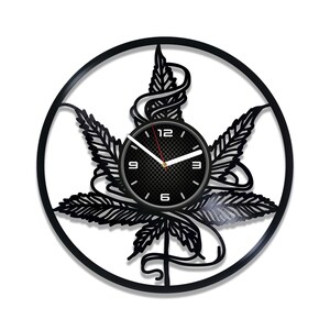 May include: Black vinyl record clock featuring a cut-out design of a marijuana leaf. The clock face has a black background with a carbon fibre pattern and white numbers.