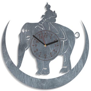 Puede incluir: Un reloj de pared de metal plateado con un diseño de media luna. La esfera del reloj está en el centro de la luna y presenta un elefante negro con un jinete en su espalda. La esfera del reloj tiene agujas negras y marcas de números romanos.