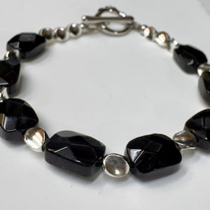 May include: A black onyx and silver bracelet with a toggle clasp. The bracelet features faceted black onyx beads and silver spacer beads.