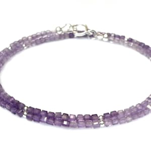 May include: A delicate bracelet featuring small, square-cut amethyst beads. The bracelet is a soft purple color and has a silver clasp. The beads are strung together to create a double-strand design, perfect for everyday wear.