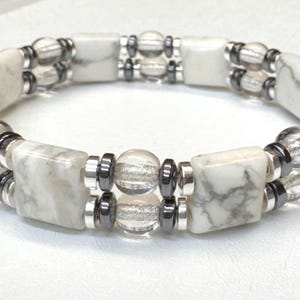 May include: White and gray marbled stone bracelet with clear and silver beads. The bracelet features rectangular and round beads, connected by silver and dark gray metal accents. A two-strand design.