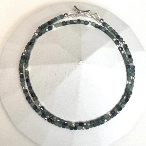 May include: A silver chain necklace with green gemstone beads. The necklace is layered with two strands of beads.