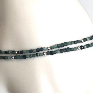 May include: A delicate bracelet made of small, square-shaped green and gray beads with silver accents.