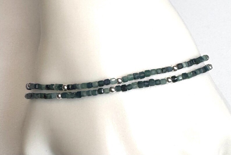 May include: A delicate bracelet made of small, square-shaped green and gray beads with silver accents.