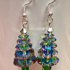 May include: A pair of Christmas tree earrings. Each earring features a tree shape crafted from iridescent, faceted beads in shades of blue, green, and purple. The earrings have silver-colored hooks.
