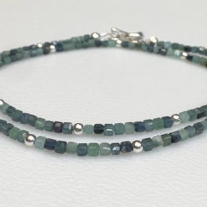 May include: A delicate double strand necklace made with small, square-shaped blue-green gemstone beads and silver spacer beads.