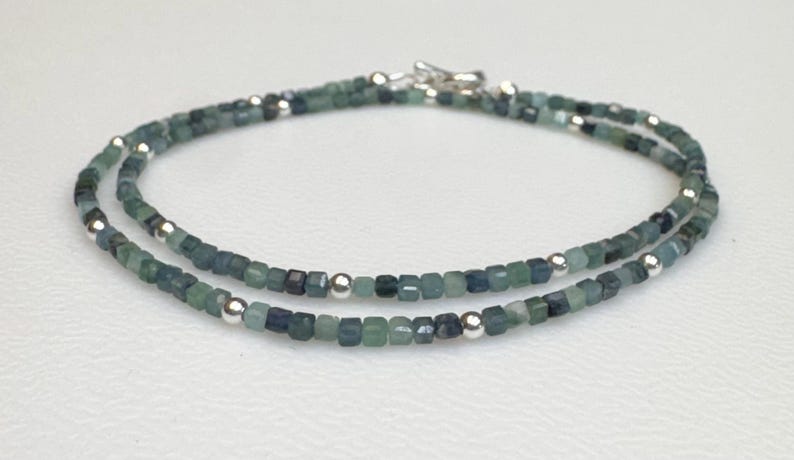 May include: A delicate double strand necklace made with small, square-shaped blue-green gemstone beads and silver spacer beads.
