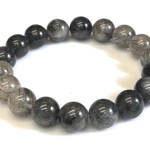 May include: A beaded bracelet featuring dark gray and clear round beads. The beads have a marbled appearance and are strung together on an elastic band. The bracelet is shown on a white background.