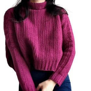 Op de afbeelding: Een magenta, cropped trui met een geribbelde textuur en een hoge coltrui. De lange mouwen en de body van de trui zijn effen van kleur. De trui is gemaakt van een zacht, gebreid materiaal.