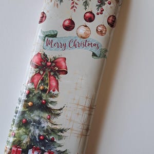 Może przedstawiać: Prostokątne opakowanie o tematyce świątecznej z uroczym wzorem. Opakowanie przedstawia choinkę, bombki i napis "Merry Christmas" na banerze. Paleta kolorów obejmuje czerwień, zieleń, złoto i biel.