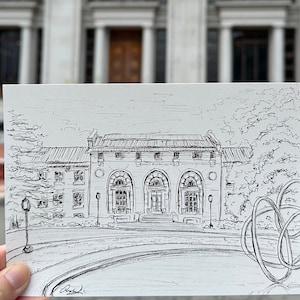May include: A black and white ink drawing of a building with arched windows and a curved driveway. The building has the text "Robert H. Jackson Center" above the entrance. The drawing is held in front of a blurred background.