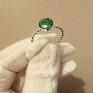 Könnte beinhalten: Ein silberner Ring mit einem runden, grünen Stein in der Mitte. Der Ring besteht aus kleinen silbernen Perlen.