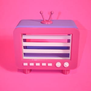 Peut inclure: Un téléviseur rétro rose et violet avec des accents blancs et un écran blanc. Le téléviseur a une paire d'antennes sur le dessus et est posé sur une surface rose.