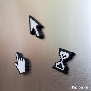 May include: Three black and white pixelated computer cursor magnets. The set includes a mouse pointer, a hand pointer, and an hourglass, all in a retro 8-bit style. The magnets are displayed on a metallic surface.