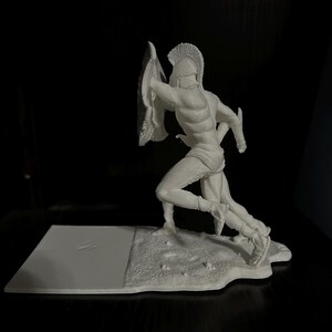 May include: A white figurine of a running Spartan warrior, complete with a helmet, shield, and sword. The figure is posed mid-stride, with detailed musculature and armor. The base is a textured, irregular shape.