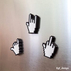 May include: Three pixelated hand gesture magnets in white and black. The gestures include the "rock on" sign, a pointing hand, and the middle finger. The magnets are displayed on a silver, metallic surface.
