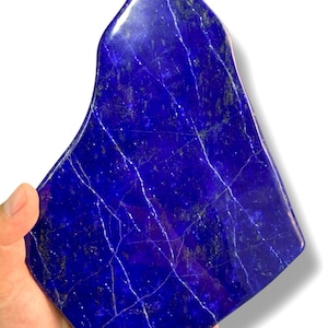 Könnte beinhalten: Eine große, polierte Lapislazuli-Platte in tiefem Blau mit weißen Adern. Die Platte hat eine unregelmäßige Form und wird in einer Hand gehalten.