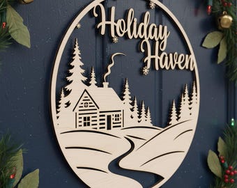 Puede incluir: Un letrero circular de madera con las palabras "Holiday Haven". El letrero presenta una escena de cabaña con árboles, un camino sinuoso y copos de nieve. Cuelga de una puerta azul, decorada con vegetación navideña.