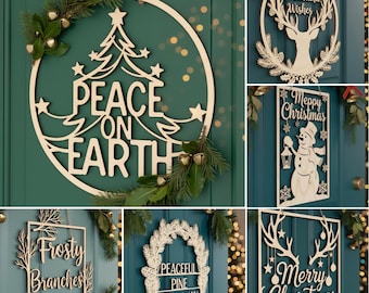 May include: A collection of wooden Christmas decorations, including wreaths and signs. The designs feature festive phrases like "Peace on Earth" and "Merry Christmas," along with images of a deer, snowman, and pine branches. Each piece is crafted from light-colored wood and adorned with greenery.