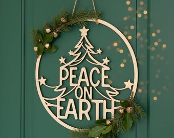May include: Wooden Christmas wreath with the words "PEACE ON EARTH" cut out. The wreath features a Christmas tree design, stars, and is decorated with greenery and small gold bells. It hangs on a green door.