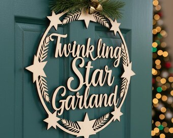 May include: A wooden star garland wreath with the words "Twinkling Star Garland" in cursive script. The wreath is decorated with star cutouts and sprigs of greenery, and is mounted on a teal door. A Christmas tree is visible in the background.